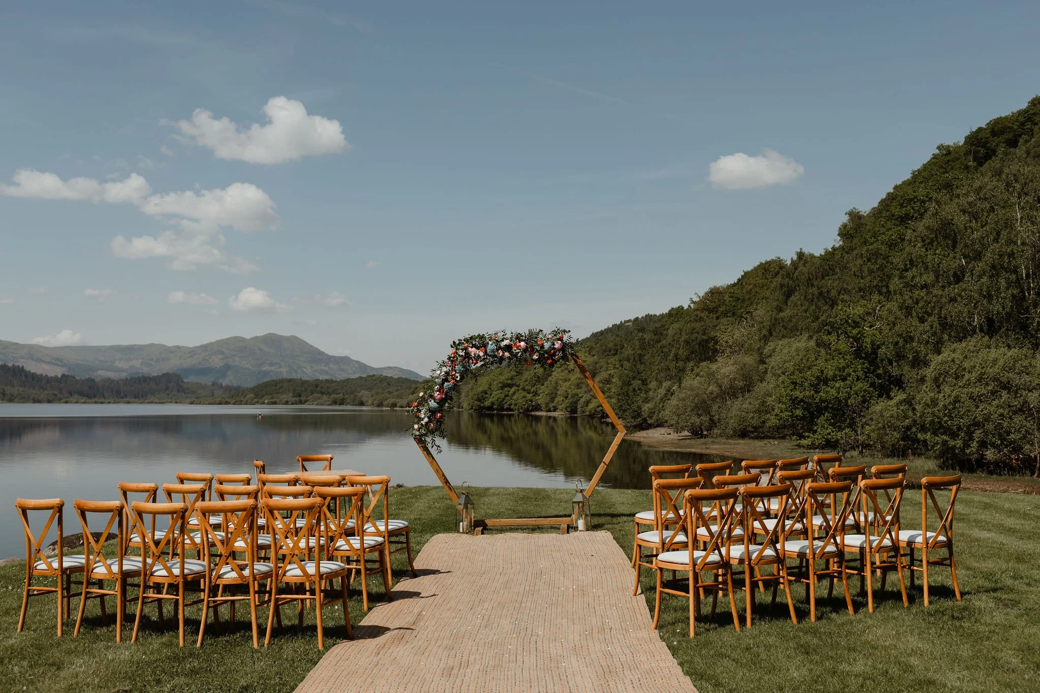 Sunny lawn ceremony setup with a floral arch over Loch Venachar